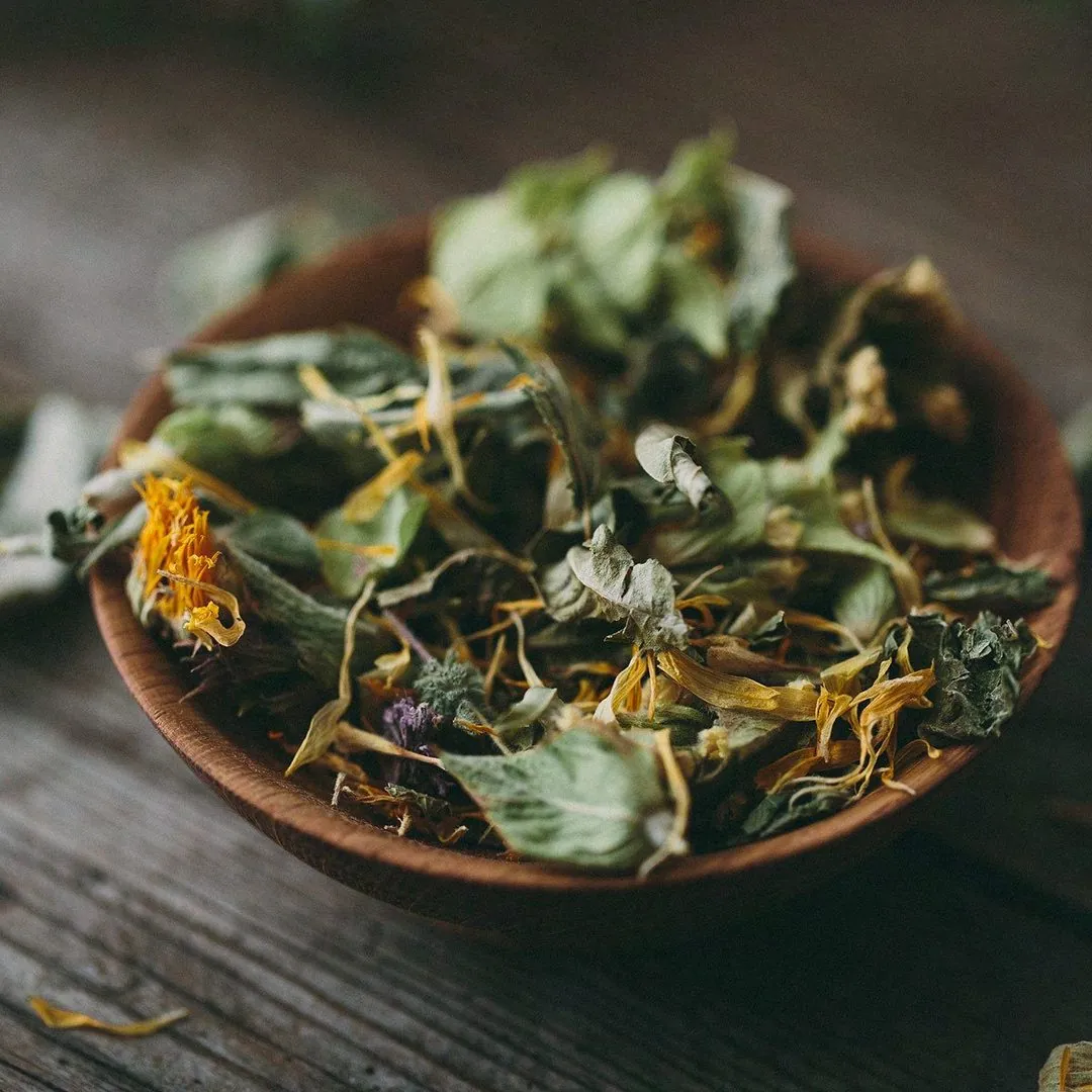 Loose leaf herbs and calendula petals in a wooden bowl
